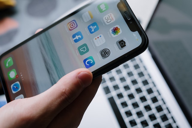 hand holding a cellphone in front of an open laptop